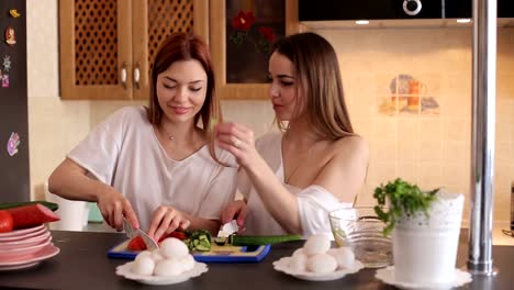 Two-friends-girls-prepare-breakfast-in-the-kitchen-and-feed-each-other-with-food