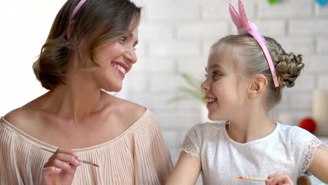 Cute-daughter-kissing-mother-on-cheek-decorating-Easter-eggs,-preparing-for-fest