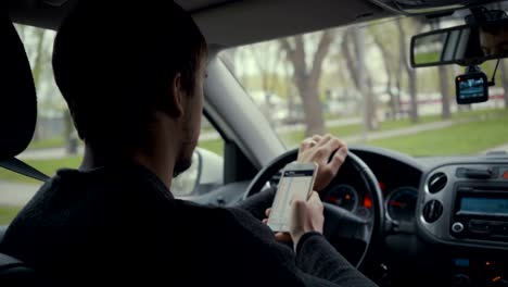 young-man-using-map-app-on-his-smartphone-in-a-car.-Footage-young-driver-behind-the-wheel.-4k