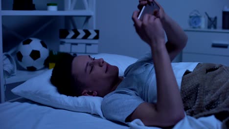 Teen-boy-making-selfie-on-smartphone-putting-it-in-bed-and-falling-asleep,-relax