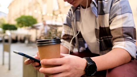 Man-using-smartphone-and-drinking-coffee-to-go-outdoor.-Close-up.-Generation-z-or-blogger,-using-his-smartphone,-scrolls-through-social-media-feed-on-device,-checking-map,-reading-news-on-app