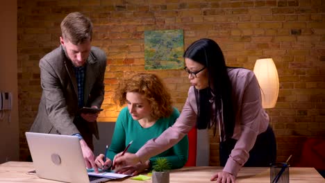 Closeup-shoot-of-three-office-workers-discussing-the-data-using-the-laptop-tablet-and-graphs-arguing-indoors-on-the-workplace