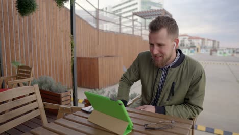 Young-man-is-communicating-by-internet-call-through-tablet-sitting-outdoors