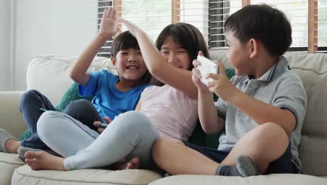 Group-of-children-friend-using-smartphone-to-play-game-together-at-home.-Children-playing-game-with-happy-emotion.