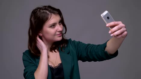 Nahaufnahme-Shooting-von-Erwachsenen-attraktiv-Brünette-weiblich,-die-Selfies-auf-dem-Handy-mit-Hintergrund-isoliert-auf-grau