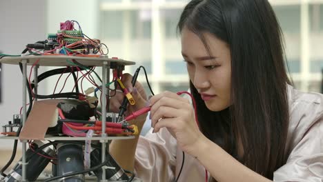 Asian-female-electronics-engineer-works-with-robot,-building,-fixing-robotics-in-workshop.-People-with-technology-or-innovation-concept.