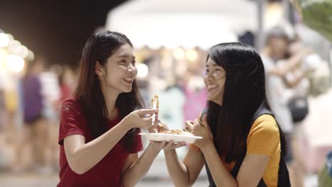 Asian-young-women-friends-travel-in-Bangkok,-Thailand,-beautiful-female-feeling-happy-walking-and-eating-Pad-Thai-at-The-Khao-San-Road.-Women-travel-eat-street-food-concept.-Slow-motion-shot.