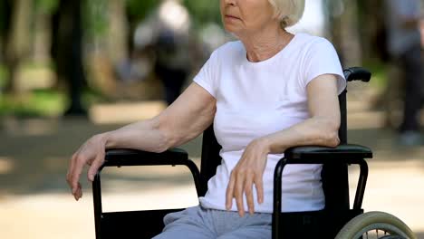 Triste-mujer-mayor-en-silla-de-ruedas-sentado-en-el-parque-mirando-a-las-personas,-discapacidad