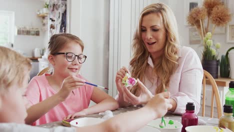 Familia-sentada-alrededor-de-la-mesa-de-la-cocina-con-los-padres-ayudando-a-los-niños-a-pintar-decoraciones-de-Pascua---tiro-en-cámara-lenta