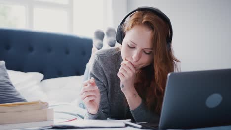 Studentin-liegt-mit-Kopfhörern-auf-dem-Bett-und-arbeitet-am-Laptop---in-Zeitlupe-aufgenommen