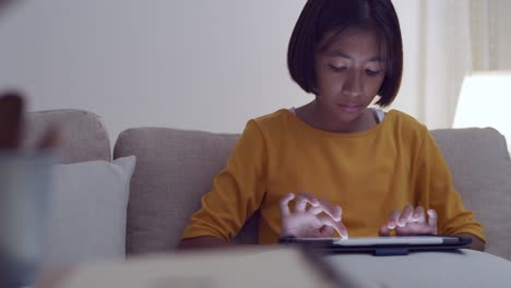 Kleine-asiatische-Mädchen-mit-Tablet-auf-Sofa-in-der-Nacht-zu-Hause