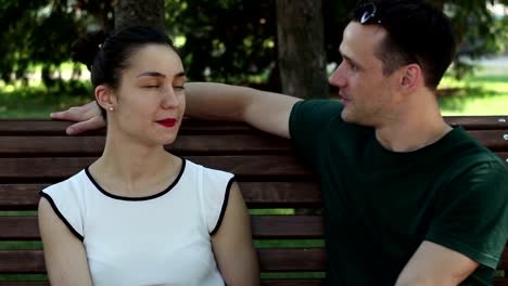 A-young-beautiful-girl-and-her-handsome-young-boyfriend-watch-the-news-in-the-social-network-on-their-smartphone-while-sitting-on-a-park-bench.