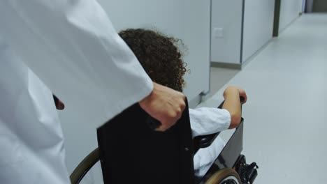 Close-up-of-Caucasian-male-doctor-pushing-pushing-African-american-boy-in-wheelchair-in-hospital-4k