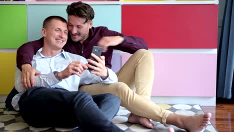 Gay-couple-using-phone-on-arm-chair-together.-Waving-bye-bye.