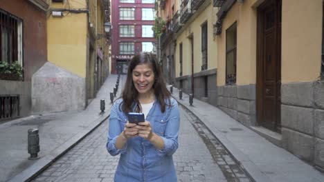 Happy-attractive-young-woman-using-smart-phone-texting-message-and-chatting-calling-friends-while-walking-on-city-street-urban-background.