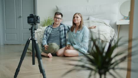 Married-couple-bloggers-recording-video-in-bedroom-talking-showing-thumbs-up