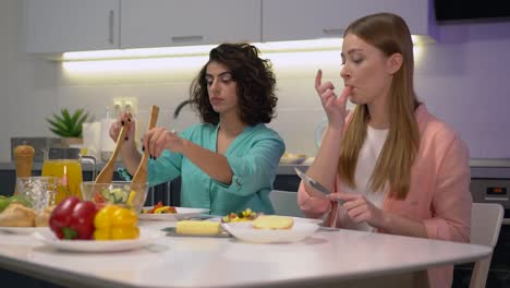 Dos-mujeres-jóvenes-almorzando-en-casa,-poniendo-ensalada-en-el-plato,-amistad