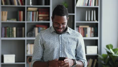 Lächelnde-afrikanische-Geschäftsmann-mit-Smartphone-im-Büro-stehen