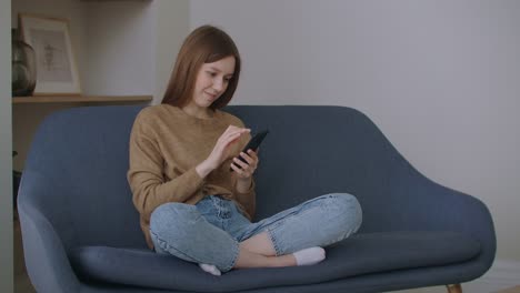 mujer-de-negocios-escribiendo-mensaje-en-el-teléfono-móvil-en-la-oficina-en-casa.-Joven-charlando-por-teléfono-en-cámara-lenta.-Cierre-las-manos-de-la-joven-usando-el-teléfono-inteligente-en-el-sofá.