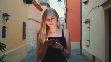 Mujer-rubia-leyendo-algo-en-el-teléfono-inteligente-mientras-camina-por-la-calle