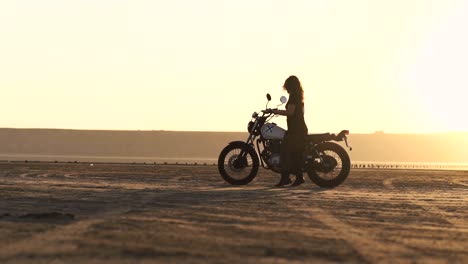 Young-beautiful-woman-goes-to-her-old-cafe-racer-motorcycle,-sits-on-it-and-makes-a-burnout,-then-rides-away.-Female-motorcycle-rider.