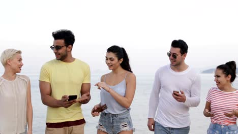 People-Walking-On-Beach-Talking-Using-Cell-Smart-Phones,-Young-Tourists-Group-Networking-Online-Laughing