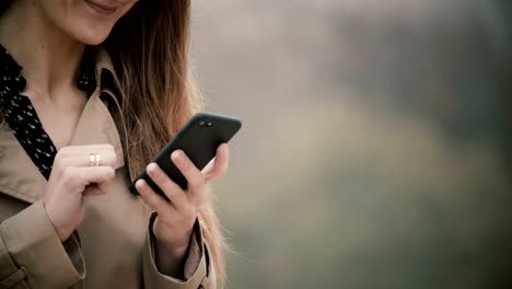 Nahaufnahme-der-weiblichen-Hände-halten-das-Handy-mit-Touchscreen.-Junge-Frau-mit-Smartphone-in-nebligen-park