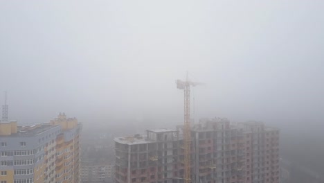 Aerial-view.-A-multi-storey-brick-house-in-the-city-in-a-fog.-A-construction-crane-is-installed-on-the-site-of-the-construction-of-a-residential-building.-New-homes-for-sale-and-rent-of-real-estate