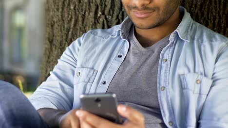 Handsome-biracial-man-smiling-and-chatting-in-social-media,-using-smartphone