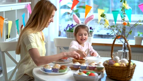 Joven-madre-y-su-pequeña-hija-con-orejas-de-conejo-divertidos-cocinar-cupcakes-de-Pascua