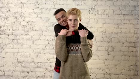 Happy-african-boy-hugging-his-beloved.-Happy-gay-couple,-lgbt-family,-white-brick-wall-on-background.-60-fps