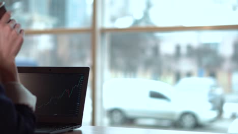 Brunette-girl-drinks-coffee-and-watches-the-exchange-chart-on-the-laptop