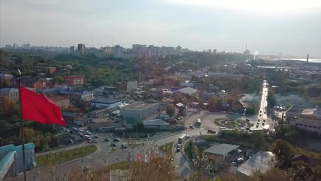 Red-waving-flag-and-beautiful-city-landscape,-top-view.-Clip.-Aerial-view-on-Russial-city-with-red-waving-flag