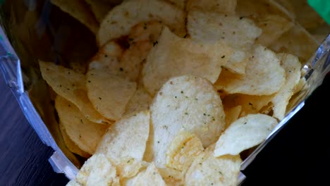 Kartoffel-Chips-im-Paket-auf-den-Tisch.-Weibliche-Hand-nimmt-chips