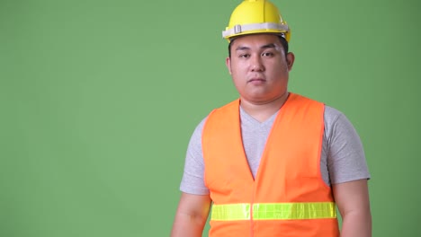 Young-handsome-overweight-Asian-man-construction-worker-against-green-background