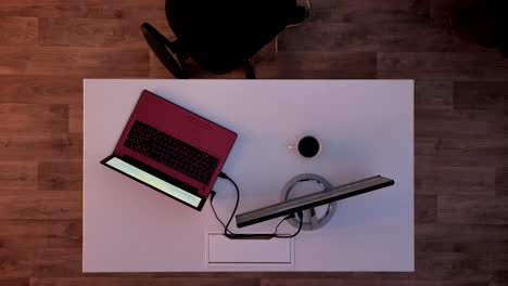 Young-man-in-glasses-and-suit-typing-on-laptop-and-going-away,-top-shot,-sitting-behind-desk-with-monitor