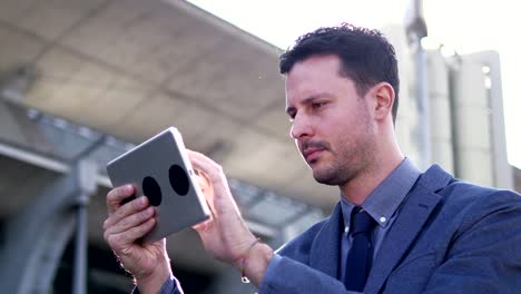 Handsome-young-businessman-writing-texts-on-digital-tablet-in-public-space