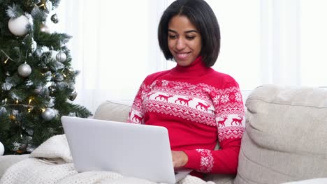 Teenage-girl-using-laptop-on-sofa-next-to-Christmas-tree-at-home