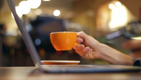 Nahaufnahme-von-Laptop-und-ein-Mann-mit-einem-Smartphone-und-Kaffeetrinken-in-einem-Coffee-shop