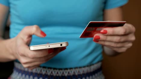 Mujer-en-una-camisa-azul-pagos-online-con-tarjeta-de-crédito-y-smartphone,-compras-en-línea,-tecnología-del-estilo-de-vida.-Chica-entra-en-el-número-de-tarjeta-de-banco-en-el-teléfono-inteligente.-Closeup.-De-cerca.