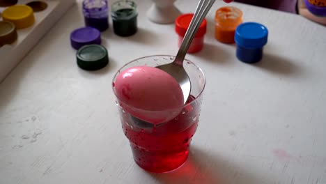 The-family-is-preparing-for-Easter,-the-child-paints-an-egg-in-a-glass-with-red-paint.-Close-up.-The-view-from-the-top.-4K.