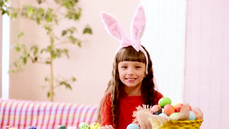 a-girl-in-rabbit-ears-looks-out-from-behind-the-table-on-which-stands-a-basket-of-Easter-eggs.