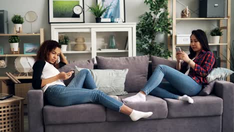 Schöne-Mädchen-Schüler-nutzen-Smartphones-mit-Gadgets-und-berührende-Bildschirme,-die-auf-Sofa-in-der-Wohnung-sitzen.-Technologien,-Menschen-und-Innenraumkonzept.