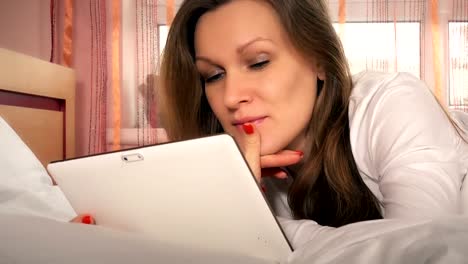 Young-happy-woman-using-tablet-computer-lying-in-white-bed