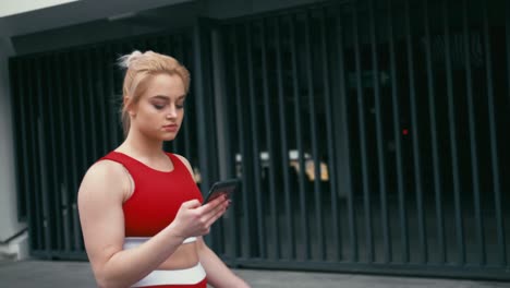 Plus-size-blond-mixed-racee-smiling-woman-wearing-red-sportswear-using-smartphone-outdoors