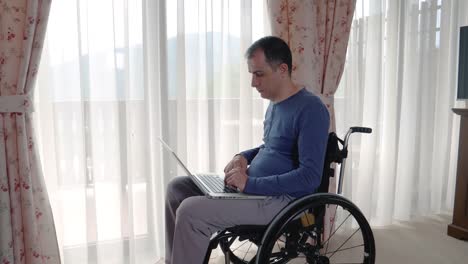 Young-man-in-wheelchair-working-at-laptop-computer-at-home