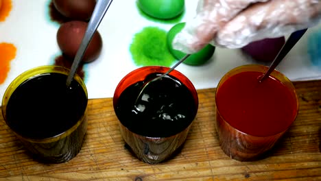 Woman-paints-Easter-eggs-in-different-colors,-dipping-them-into-cups-with-multicolored-dyes.