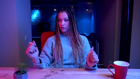 Closeup-shoot-of-young-attractive-female-blogger-with-dreadlocks-streaming-live-and-talking-cheerfully-with-the-neon-background-indoors