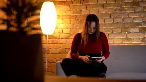 Closeup-shoot-of-young-pretty-caucasian-female-typing-on-the-tablet-while-sitting-on-the-couch-indoors