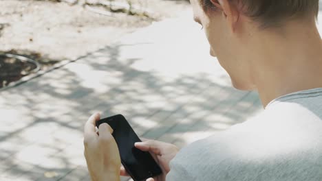 Mann-chattet-auf-Handy.-Entspannter-Kerl-sitzen-und-Blick-auf-Handy-in-City-Park.-Schöne-männliche-Chat-mit-Smartphone-im-Freien.-Mann-chattet-mit-Freund.